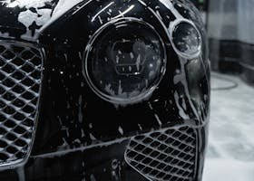 Close-up of a sleek black luxury car with soapy foam during a carwash process.